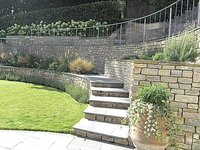 Large sloping garden design in Kenley, Surrey with stone faced retaining walls and stainless steel railings.