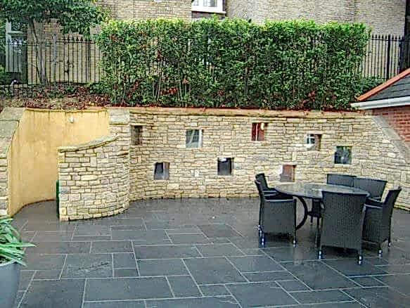 Large sloping garden design in Kenley, Surrey with stone faced retaining walls and curved cooking area..
