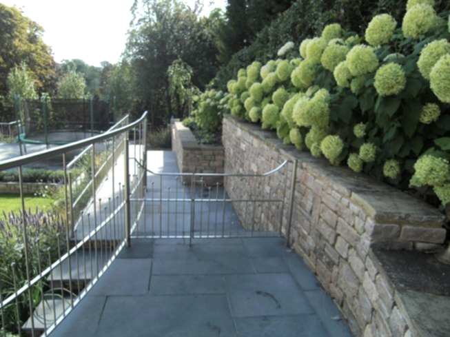 Large sloping garden design in Kenley, Surrey with stone faced retaining walls and stainless steel railings.