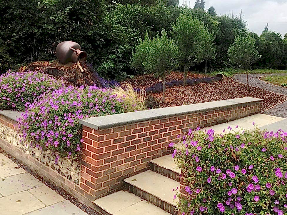 Garden design in Denham, Buckinghamshire with flint and brick walls and steps up into woodland.